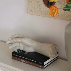 Statue of a hand on a book with a decorative painting in the background