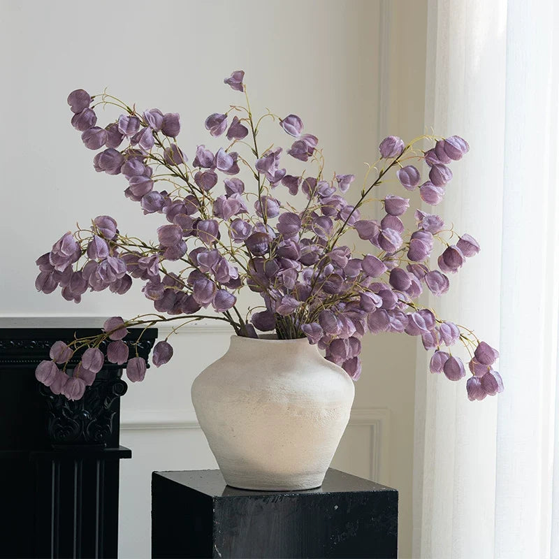 Vase with purple flowers on a black surface against a white wall